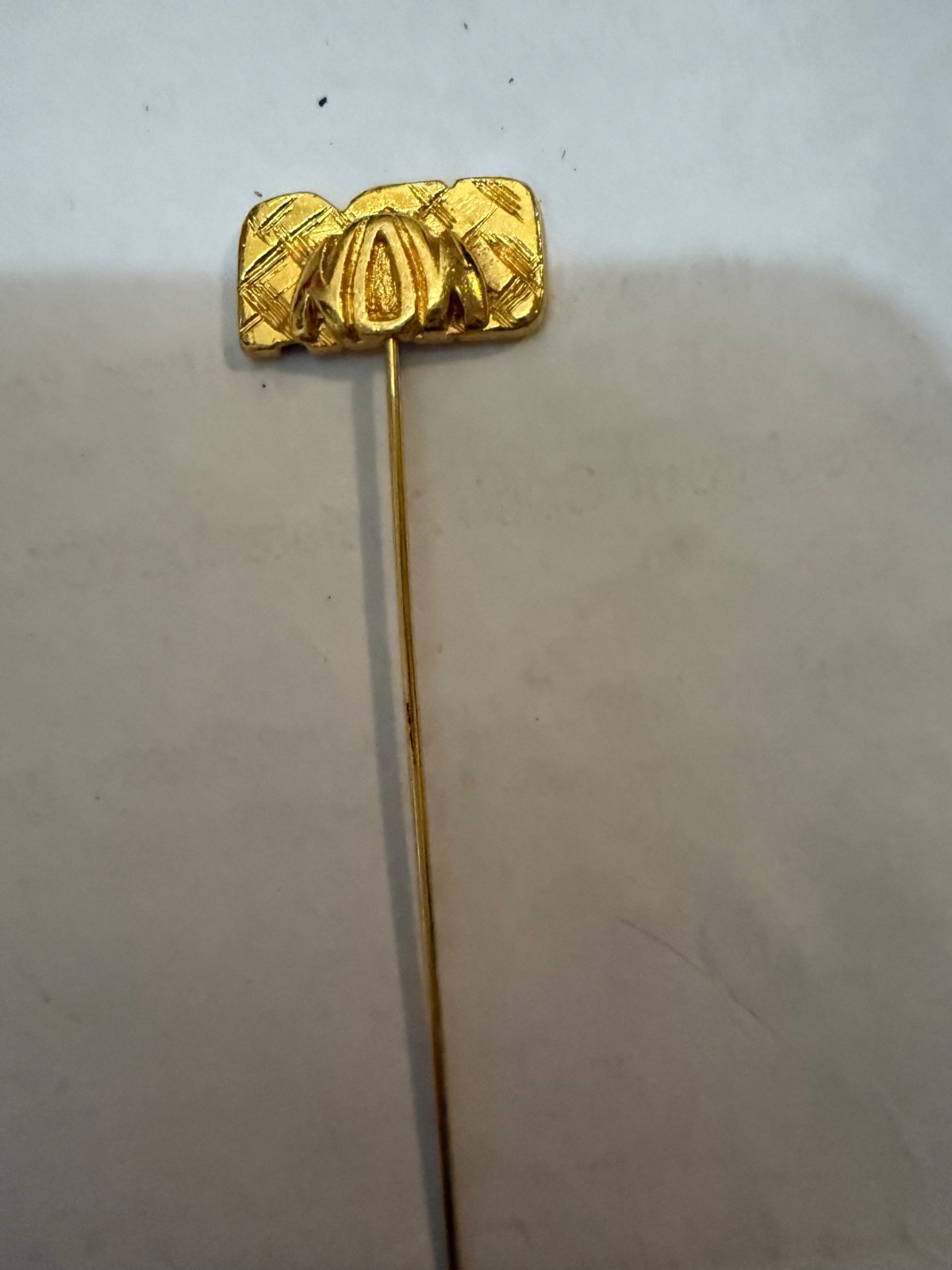 gold-tone “ERA” stick pin, a type of decorative accessory typically worn on lape