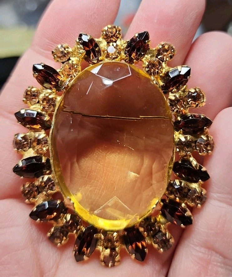 A vintage gold-tone brooch featuring a large, faceted yellow central stone.