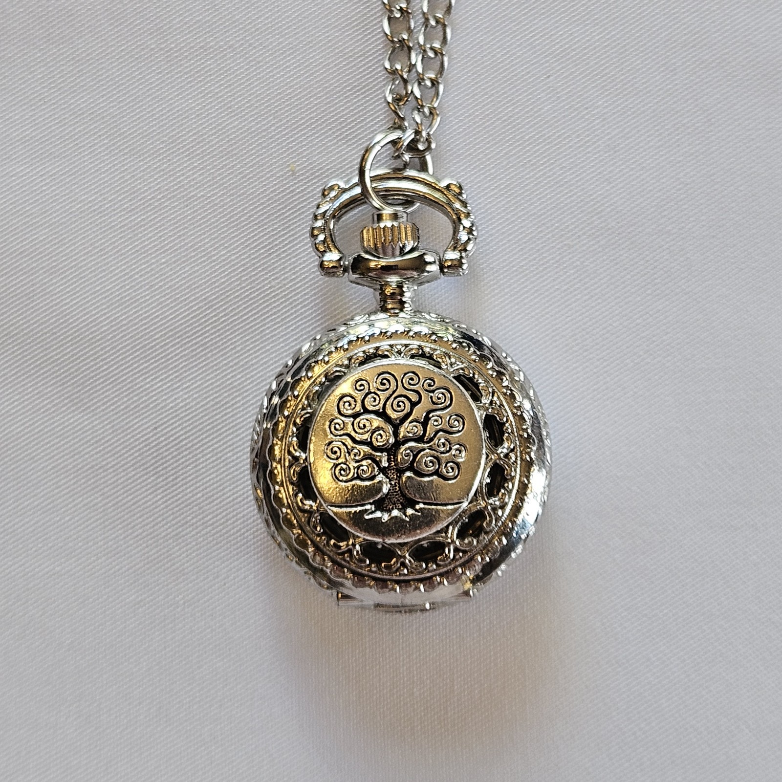Silver-toned quartz pocket watch necklace with a filigree design.
