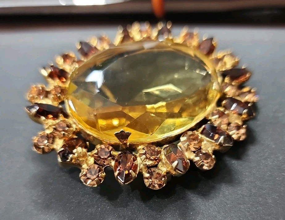 A vintage gold-tone brooch featuring a large, faceted yellow central stone.