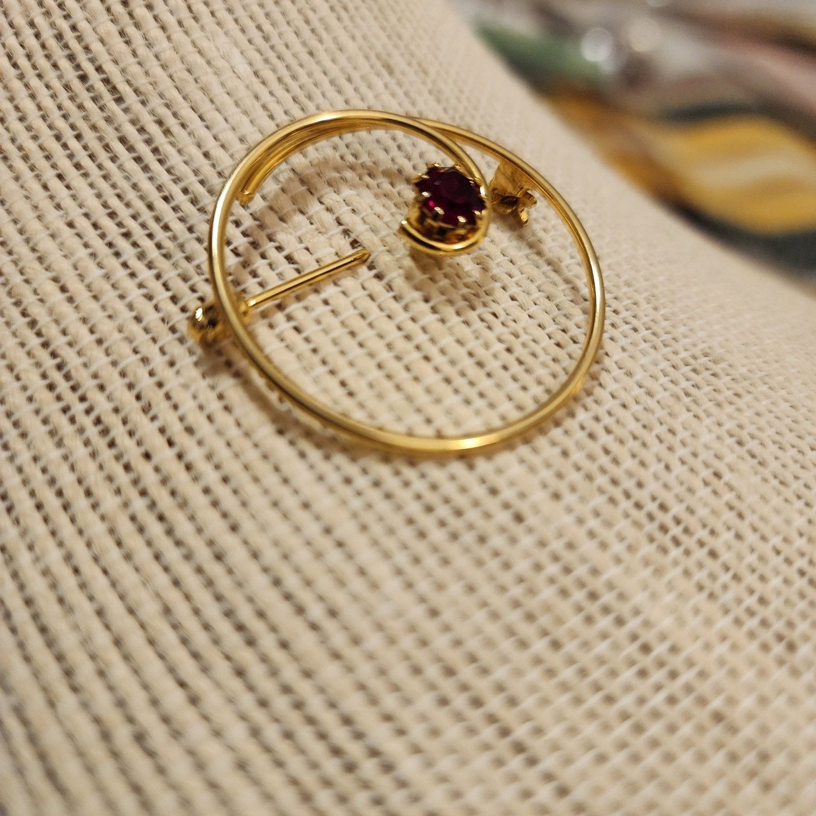 Gold Tone Swirl Circle Brooch With Red Rhinestone Accent.