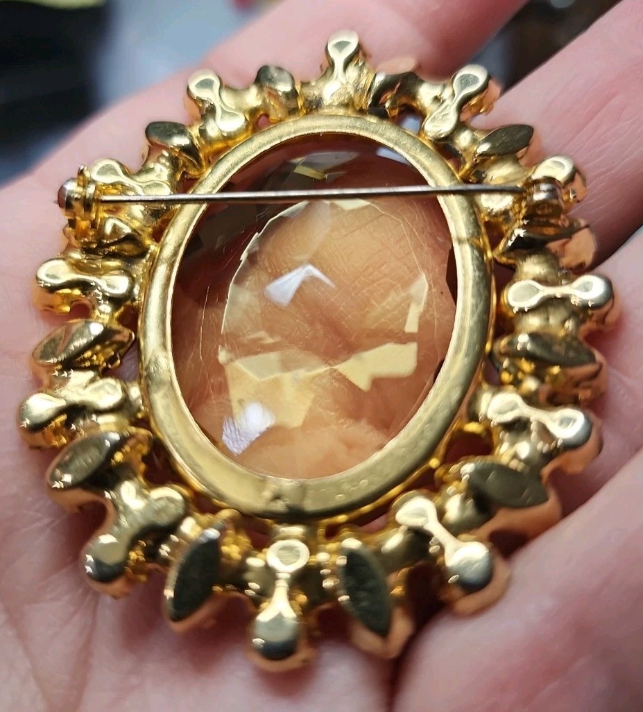 A vintage gold-tone brooch featuring a large, faceted yellow central stone.