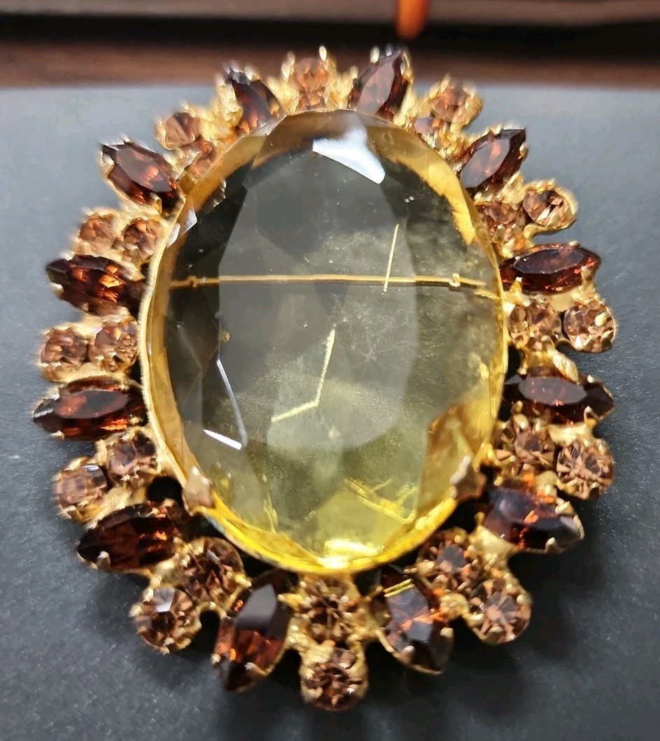 A vintage gold-tone brooch featuring a large, faceted yellow central stone.