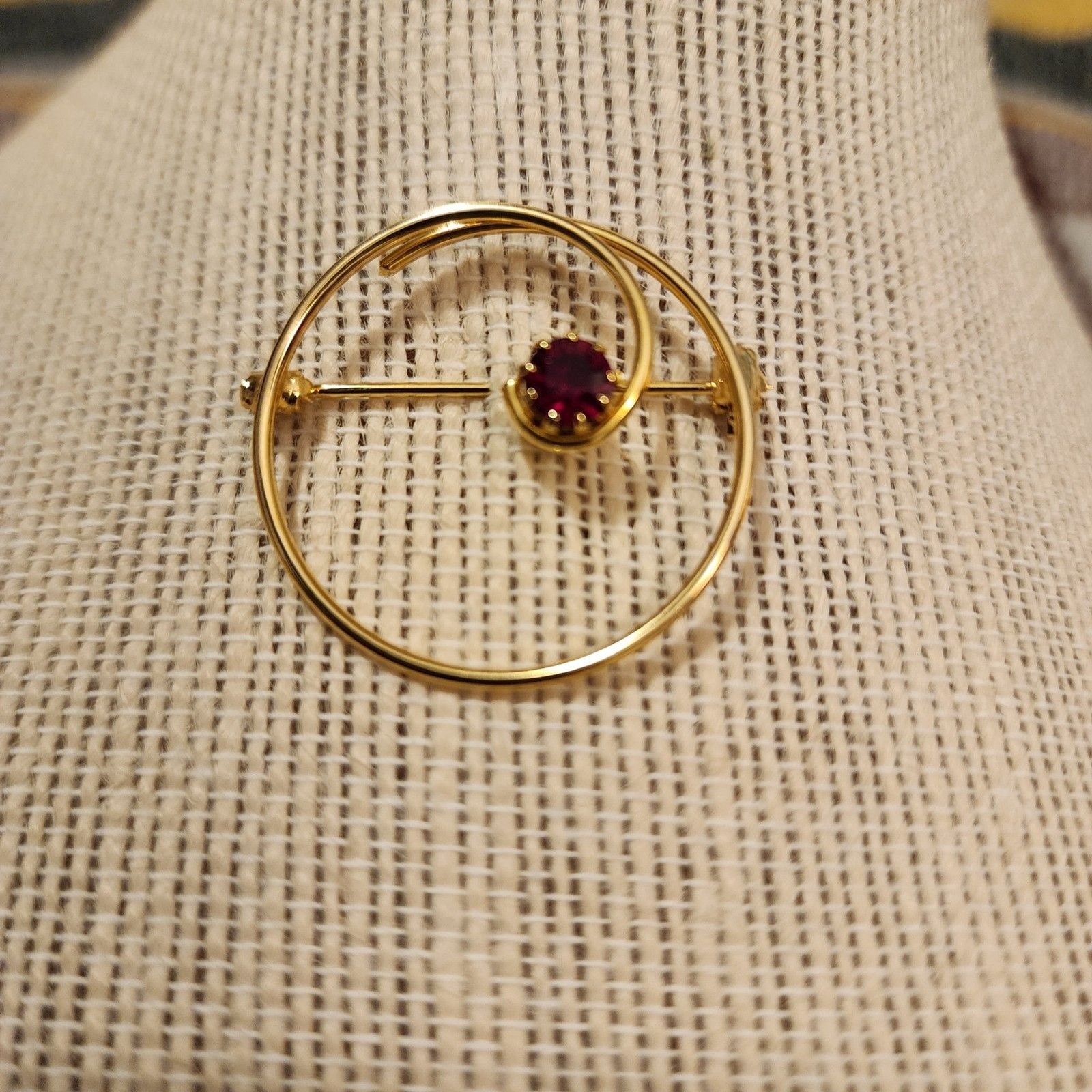 Gold Tone Swirl Circle Brooch With Red Rhinestone Accent.